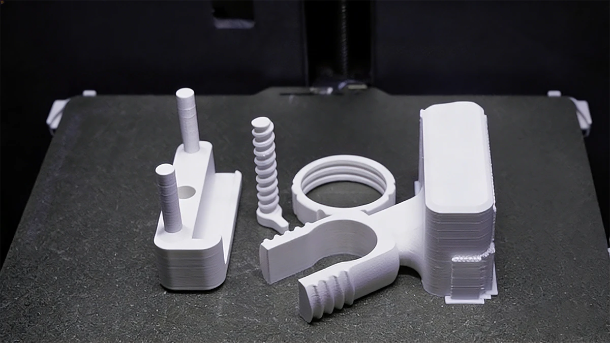 Display of 3D printed white functional parts (jigs, brackets, springs) made with NextShapes PETG HF filament, showcasing structural stability and dimensional accuracy
