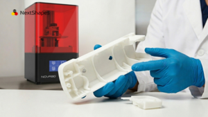 Engineer with blue nitrile gloves inspecting 3D printed electronics enclosure prototype made from NextShapes ABS Like Plus resin beside desktop SLA printer, showing functional prototype application for product validation